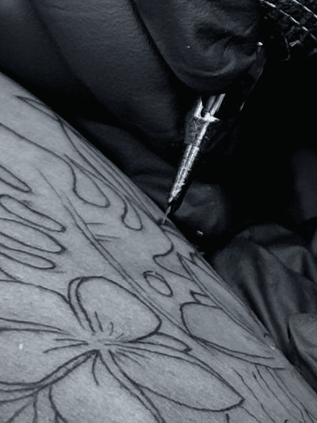 Schwarz-weiße Detailaufnahme einer Tattoo-Nadel während des Tätowierens im Arbeitsprozess.