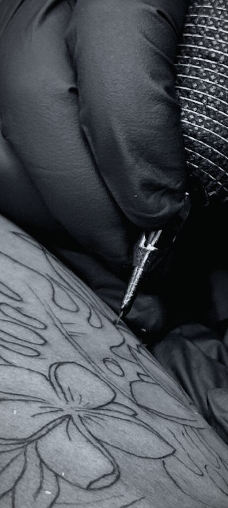 Detailaufnahme einer Tattoo-Nadel beim präzisen Nachziehen floraler Linien auf der Haut