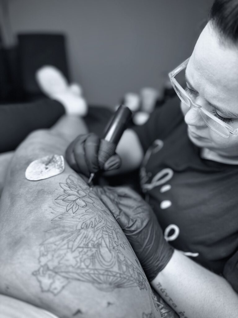 Schwarz weiß Aufnahme eines Tattoo Artist bei der Ausarbeitung eines floralen Tattoos