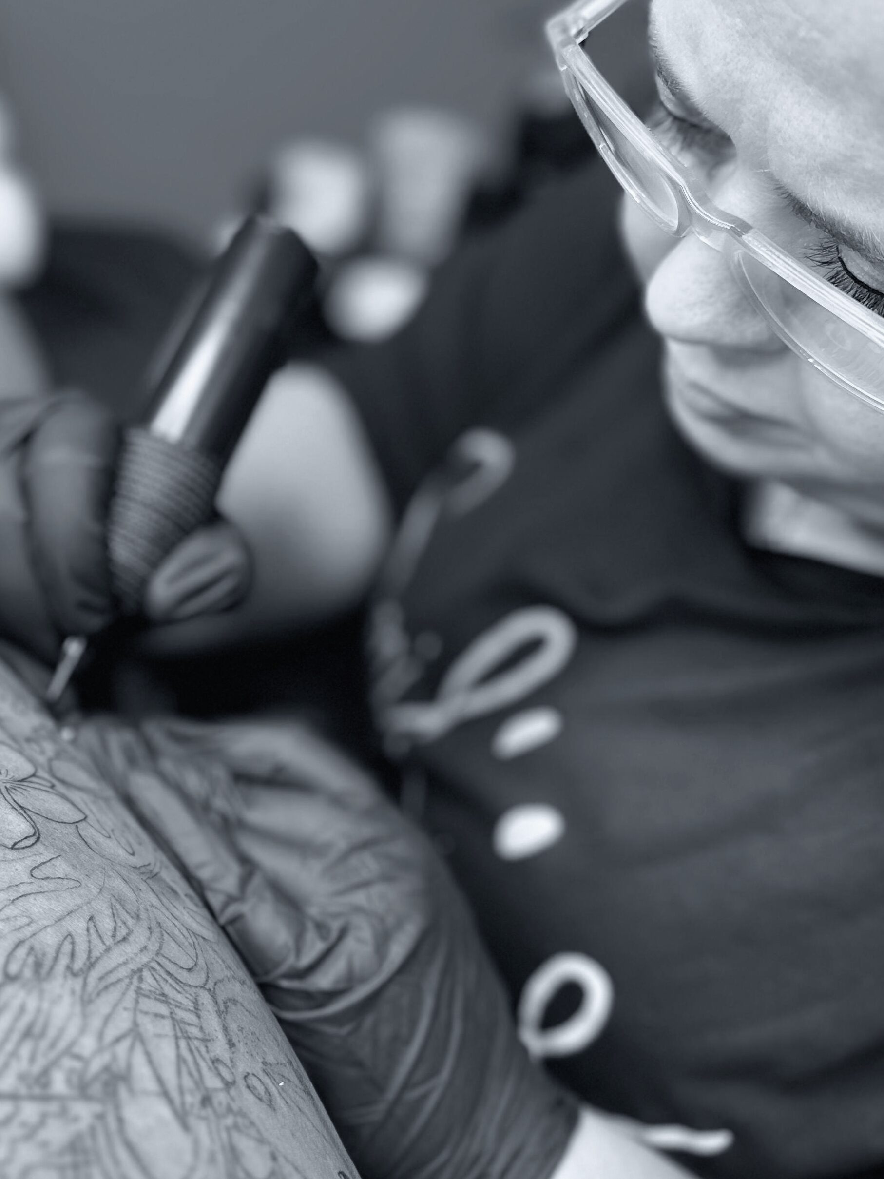 Schwarz weiß Aufnahme eines Tattoo Artist bei der Ausarbeitung eines floralen Tattoos