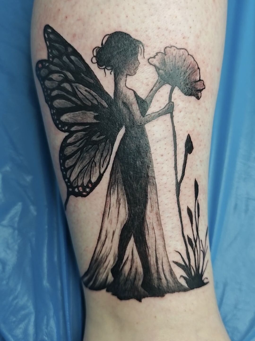 Frisch gestochenes Tattoo einer Fee mit Mohn-Blume am Unterschenkel
