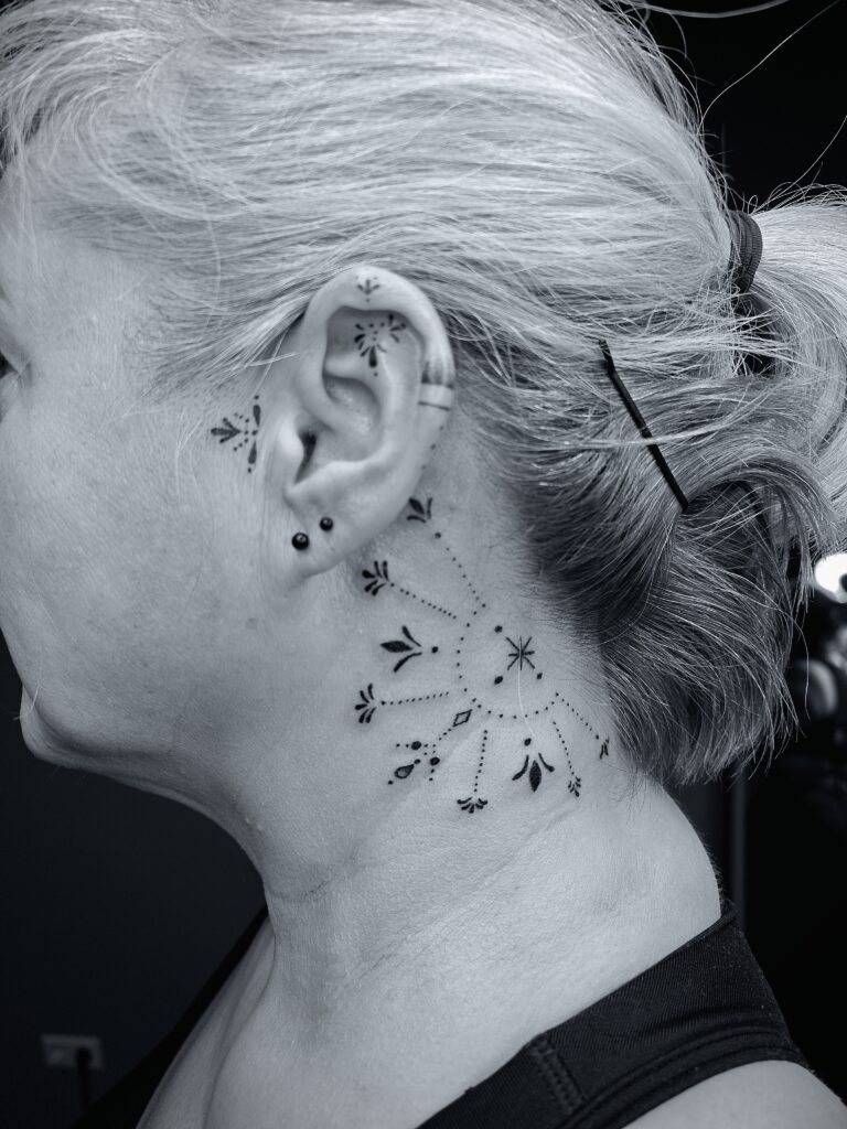 Eine beliebte Tattoo Stelle am und hinter dem Ohr mit einem femininen ornamental Fineline Motiv.